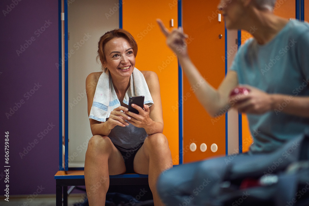 Φωτογραφία Beautiful young woman in sportswear sitting in gym locker room and enjoying conversation with her friend