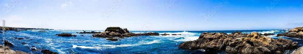 Panoramic shot of beautiful rocky coastline and undulating ocean in harmony with blue sky