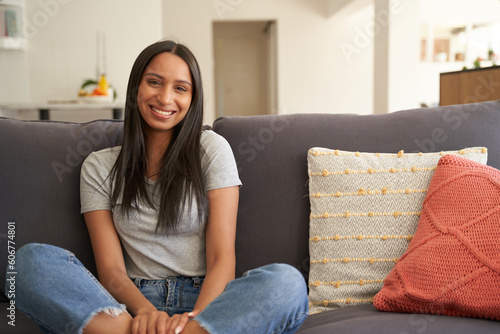 Happy young biracial woman in casual clothing smiling while sitting on sofa in living room at home