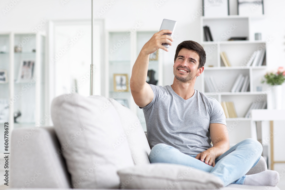 Young handsome happy man talking on a video call or takes a selfie on sofa in living room. Young handsome happy man talking on a video call or takes a selfie on sofa in living room.