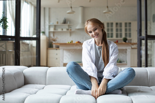 Young beautiful woman in casual clothes is sitting on the sofa in the living room smiling looking at the camera
