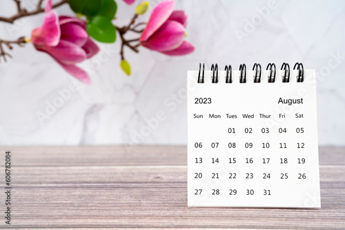 The August 2023 desk calendar and white pink magnolia flower on wooden background.