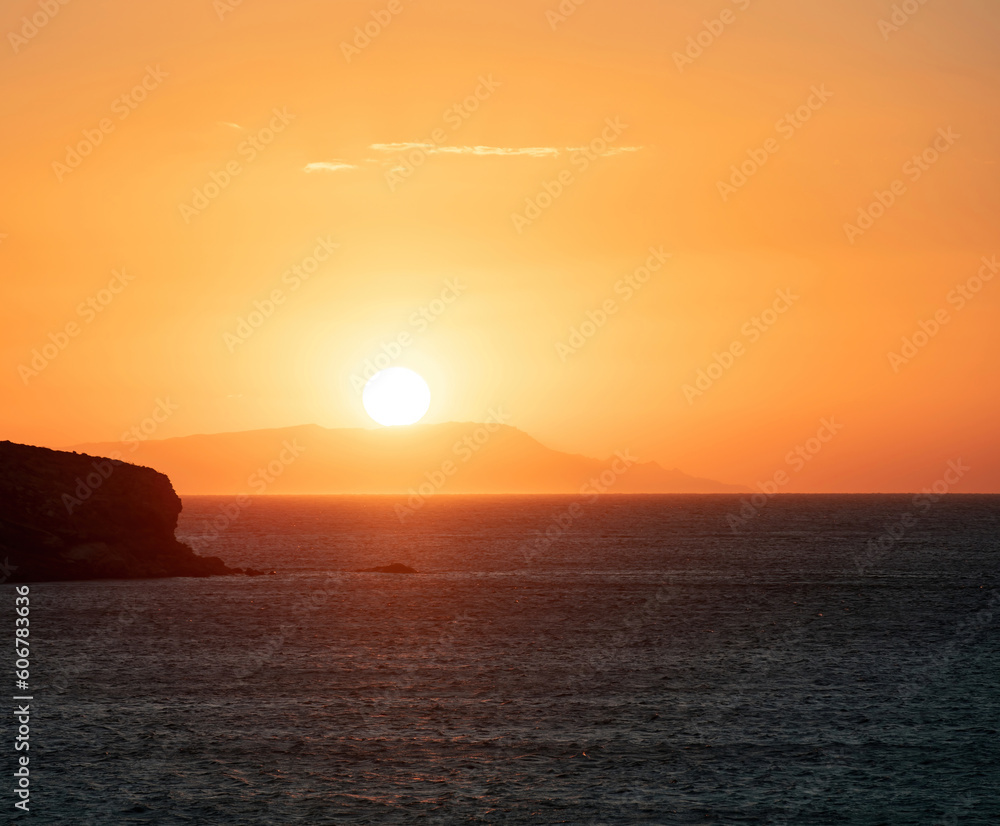 Sunset over Greek island, Cyclades, Greece. Golden sun colors the sky. Calm vast Aegean sea.