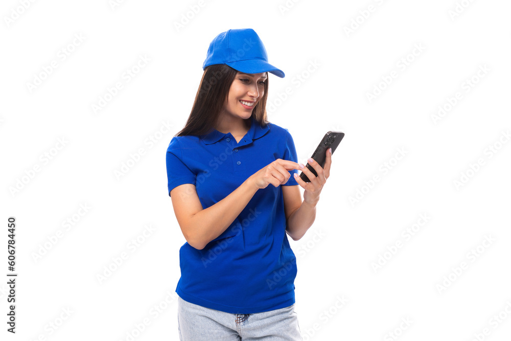 young caucasian brunette woman in blank blue t-shirt and cap uses smartphone young caucasian brunette woman in blank blue t-shirt and cap uses smartphone