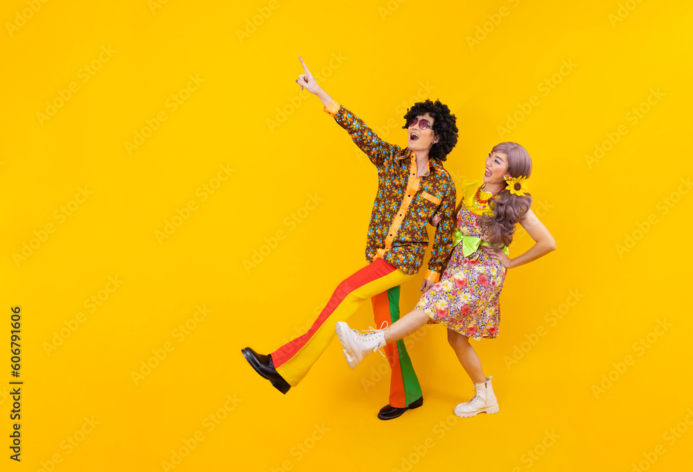 Asian hippie couple dress in 80s vintage fashion with colorful retro clothing while dancing together isolated on yellow background for fancy outfit party and pop culture concept - obrazy, fototapety, plakaty 