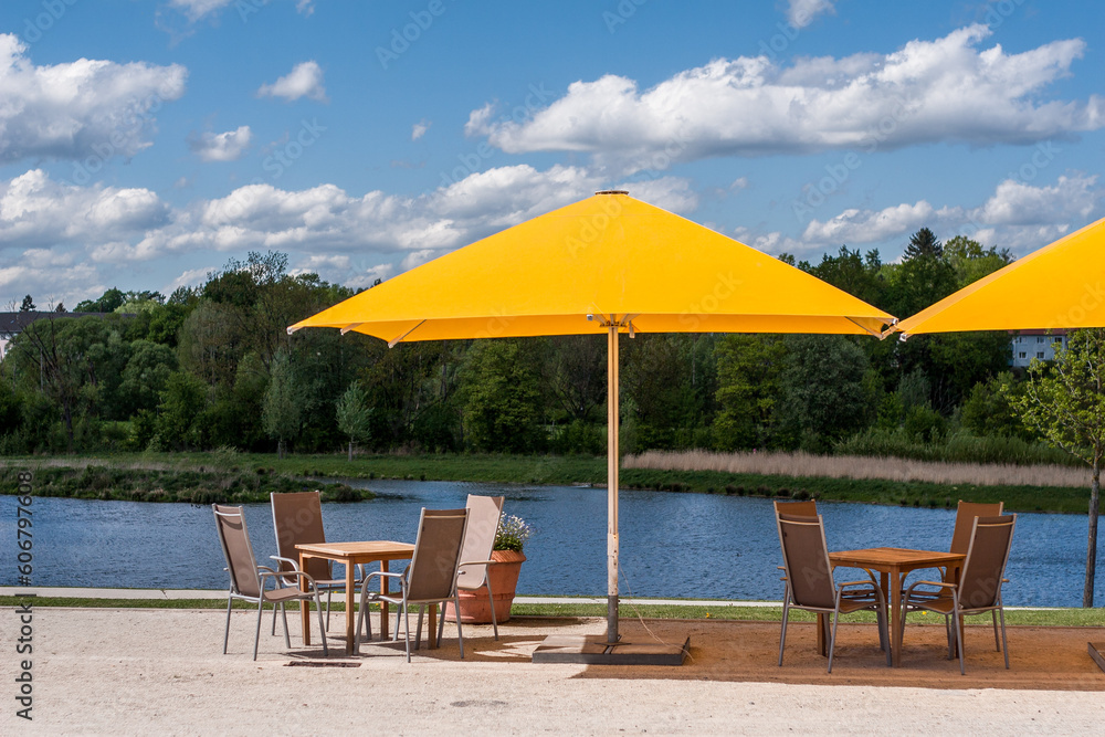 Gastronomie mit Sonnenschirm, Tisch Stühlen an einem See mit blauen Wolken