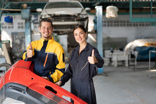 Portrait Caucasian man and woman mechanic thump up and holding red bumper car with car lift background at car service 