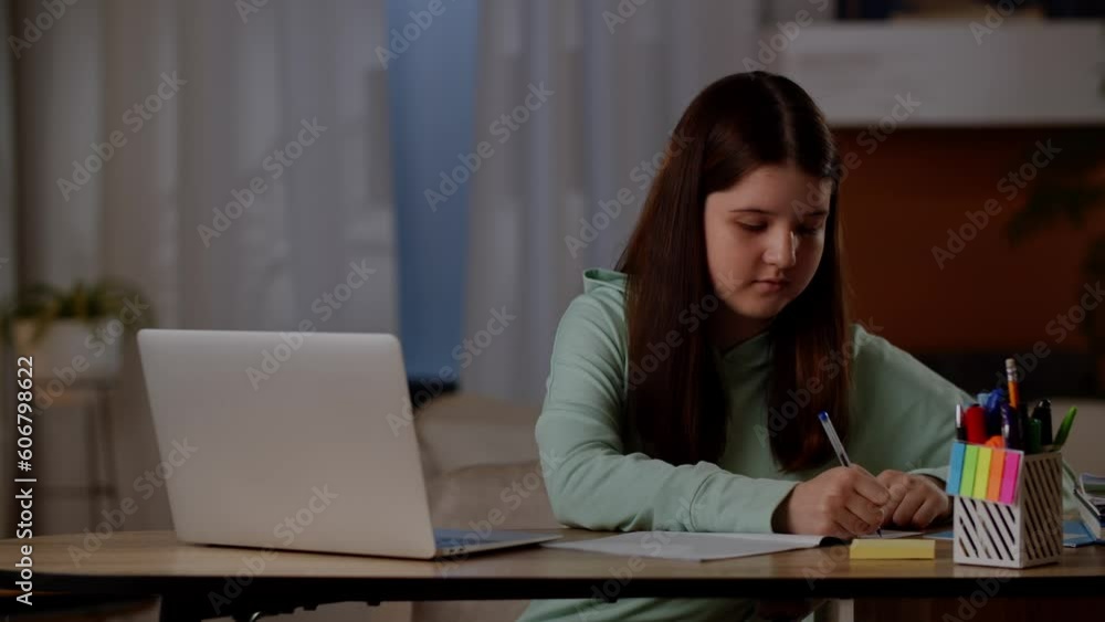 A girl sits at a table in front of a laptop and writes something in a notebook. A girl uses a laptop to search the Internet for material to do her homework. A girl sits at a table in front of a laptop and writes something in a notebook. A girl uses a laptop to search the Internet for material to do her homework.