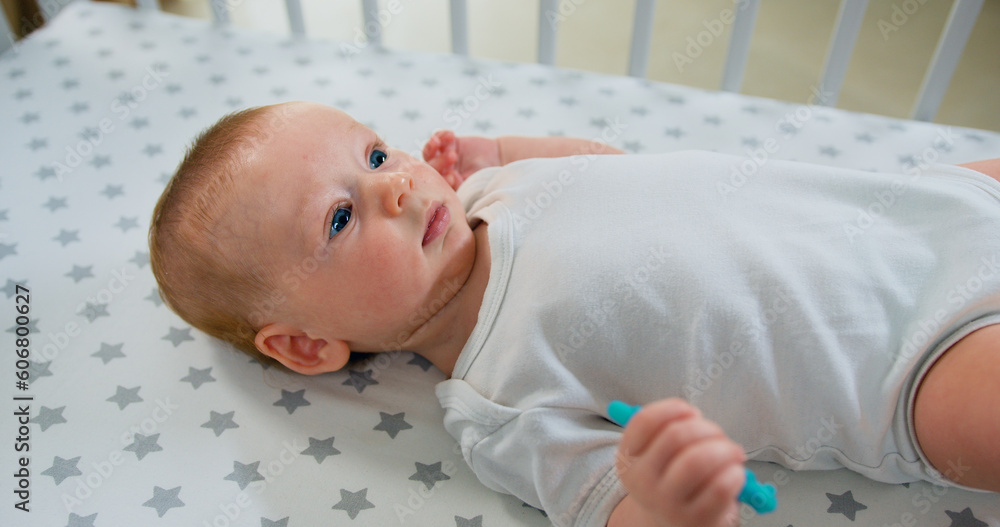 Close up of sweet beautiful newborn baby in bodysuit and diaper lying on bedsheets. Portrait little caucasian boy is funny smiling, lying at the back in the child crib. Close up of sweet beautiful newborn baby in bodysuit and diaper lying on bedsheets. Portrait little caucasian boy is funny smiling, lying at the back in the child crib.