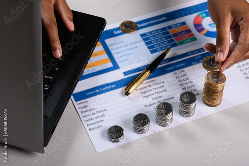 A person is using a laptop computer to check a stack of Brazilian coins on a shopping list photo