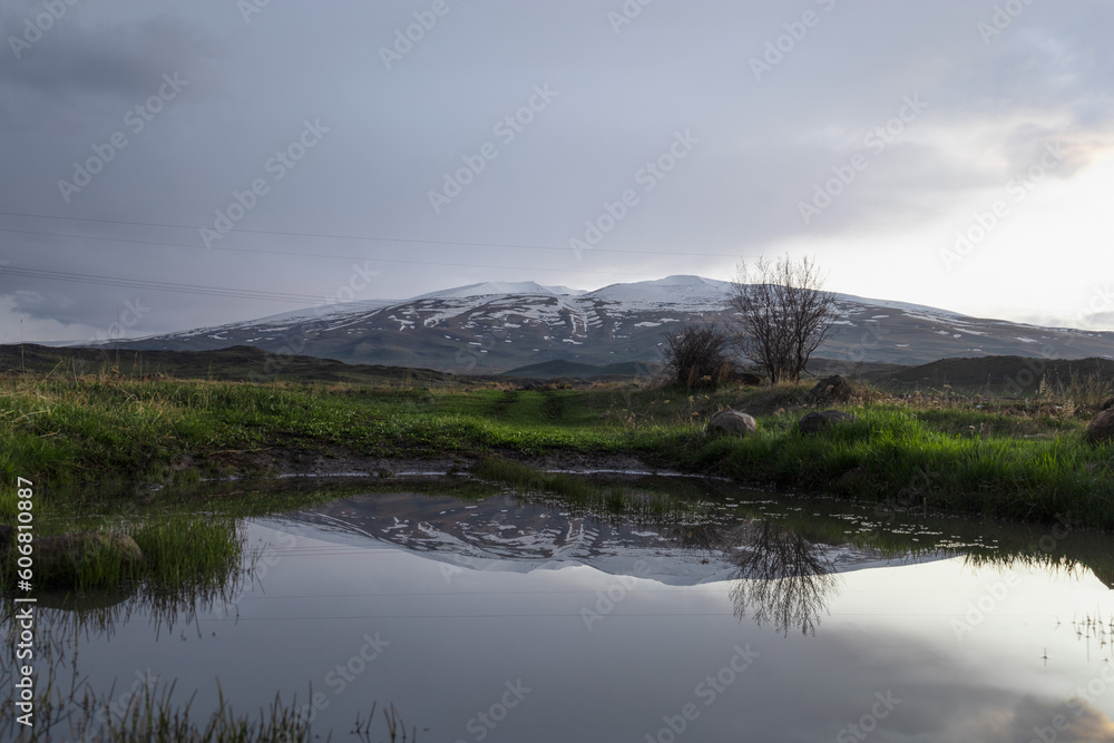 Spectacular view of Mount Aragats partially covered with snow, reflected in a water pool in a spring day, during sunset