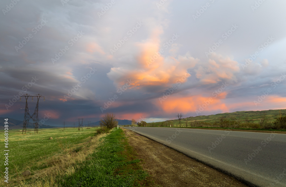 Scenic perspective of an empty highway against a vibrant backdrop of dramatic, colorful clouds during the golden hour