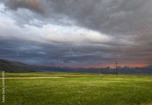 Spectacular view of a lush green field against the majestic backdrop of mountains and dramatic colorful clouds during sunset