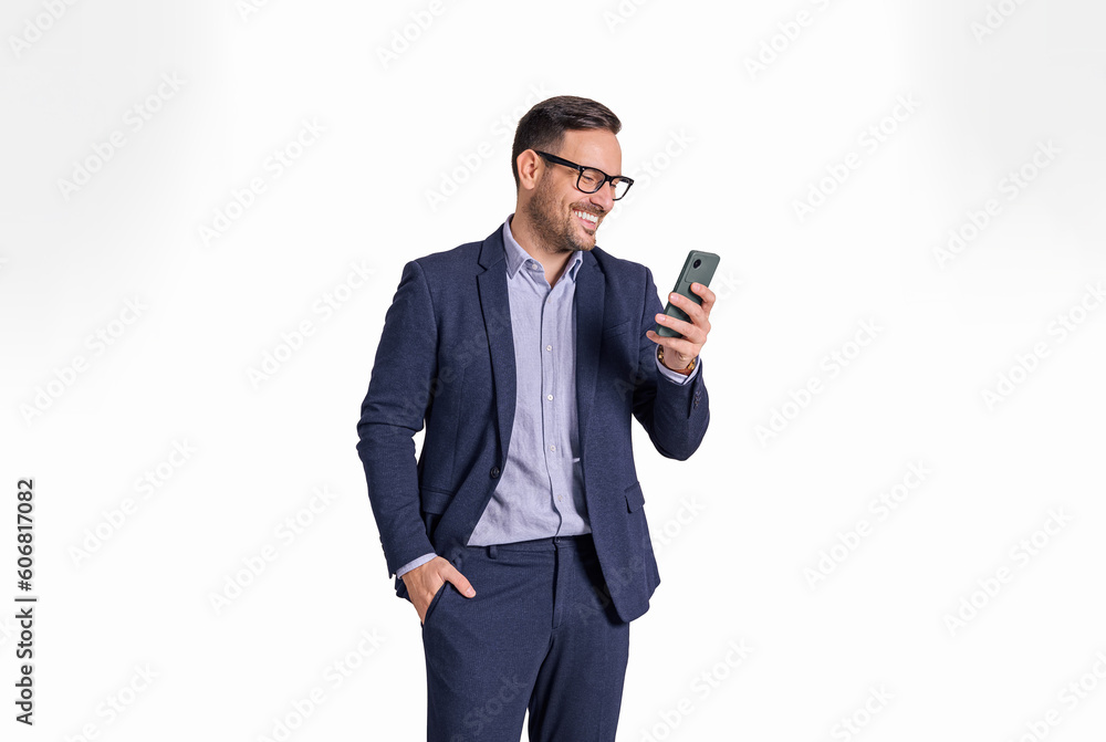Handsome male professional manager with hand in pocket messaging online on mobile phone. Elegant businessman reading e-mails on cellphone while standing isolated over white background Handsome male professional manager with hand in pocket messaging online on mobile phone. Elegant businessman reading e-mails on cellphone while standing isolated over white background