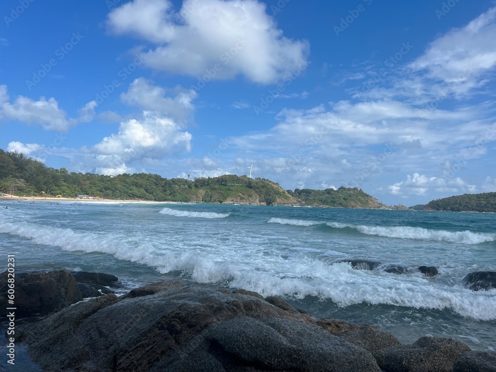 Wave with white foam on the sandy beach at Naiharn with rocks and blue sky with sun and palm trees