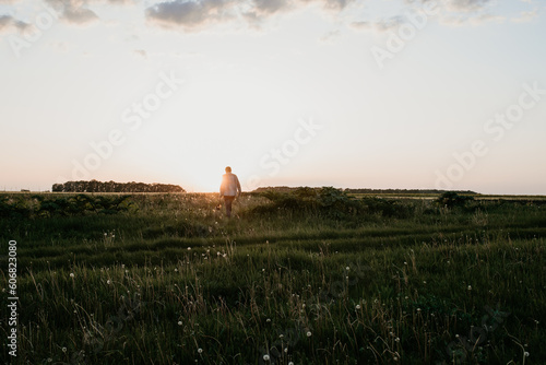 lonely boy walks across a field at sunset