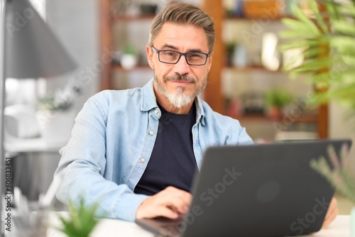 Fotobehang Casual mid adult man with laptop computer at desk in home office, banking online, remote working