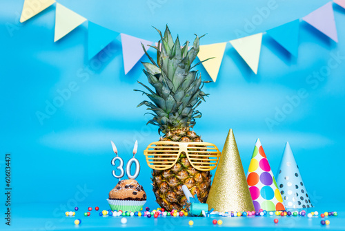 Creative background with pineapple character in sunglasses copy space. Happy birthday background with muffin or cake with candle number  30. Anniversary holiday decorations on a blue background.