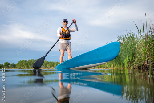senior male paddler is paddling a stand up paddleboard on a calm lake in spring, frog perspective from an action camera at water level