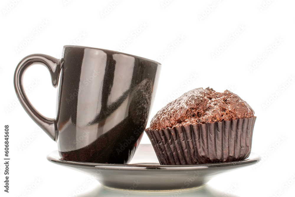 One homemade chocolate muffin on a saucer with a black cup, macro, isolated on white background. One homemade chocolate muffin on a saucer with a black cup, macro, isolated on white background.