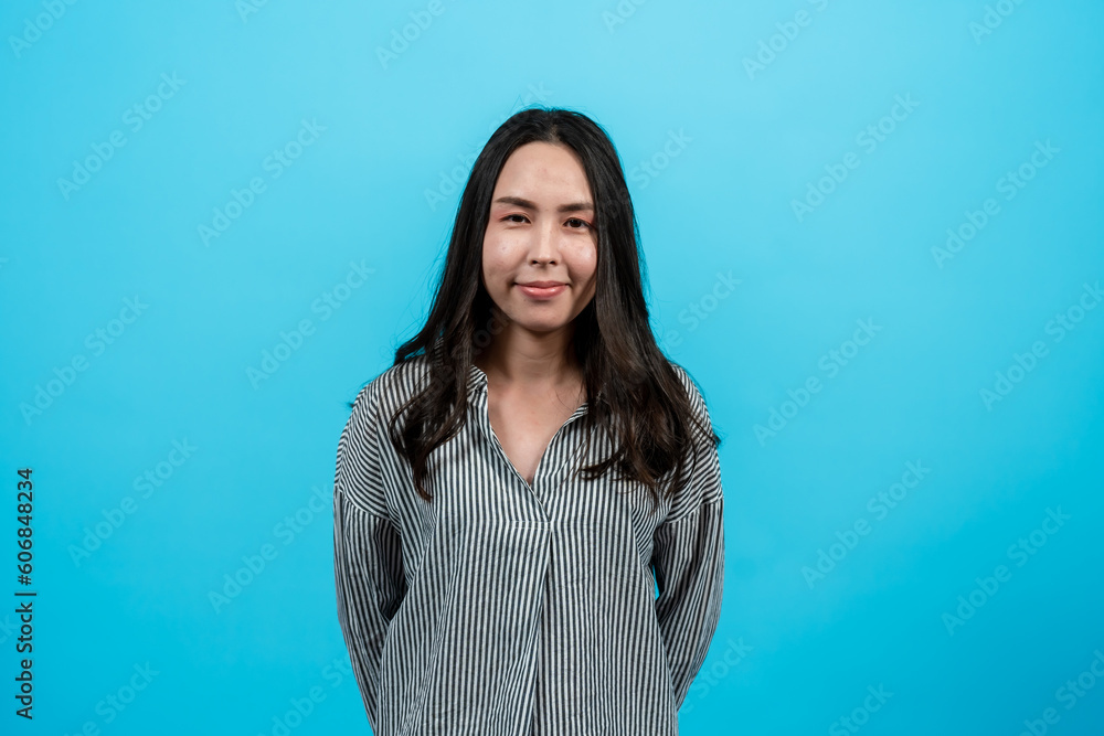 Obraz premium Portrait Asian woman in casual shirt with long sleeves looking straight ahead. Smile at the camera that is capturing it. Indoor studio isolated on blue background