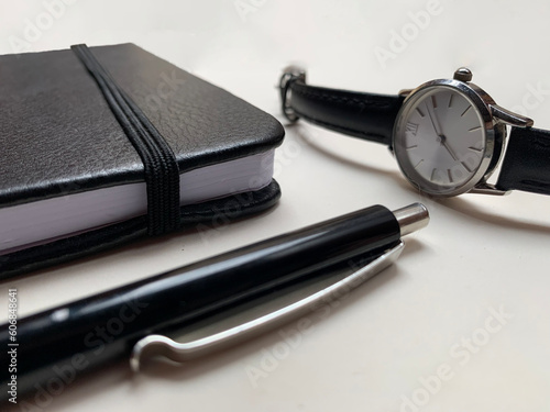 black notebook  black pen  watch. On a white background