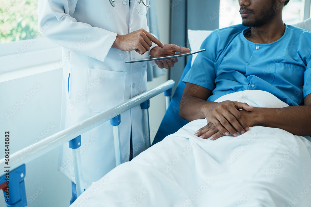 Friendly Male Doctor Talks to Male Patient Resting in Bed. doctor with chart attending sick man in hospital ward. Friendly Male Doctor Talks to Male Patient Resting in Bed. doctor with chart attending sick man in hospital ward.