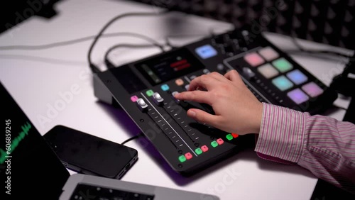 Side angle of unrecognized female podcaster operating a soundboard on white desk for a podcast recording in acoustic studio