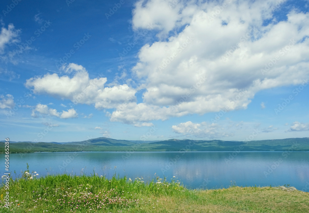 Beautiful blue lake, grass shore and big clouds in sky, abstract natural background. Summer landscape. atmospheric scenic view. travel, adventure, vacation concept. Russia, South Ural, lake Turgoyak.