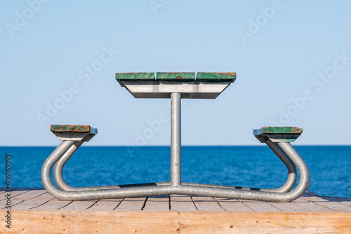 Canvas Print metal and wood picnic bench seen end on with water horizon line and sky in background