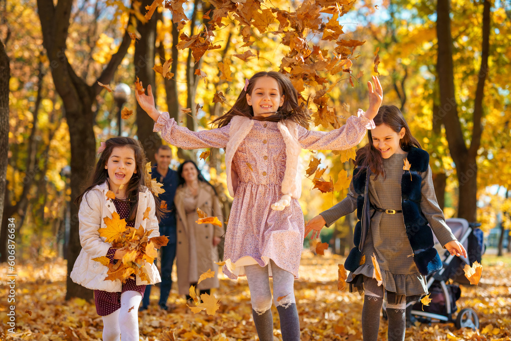 Fototapeta premium happy children playing together and scattering yellow leaves, portrait of big family in autumn city park, children running with armful of leaves, beautiful nature, bright sunny day