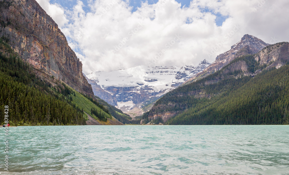 Lake Louise, Banff National Park, Alberta, Canada. The lake is located in the Canadian Rockies. panorama of snow-capped mountain peaks, coniferous forest and blue glacial lake, cloudy day. 