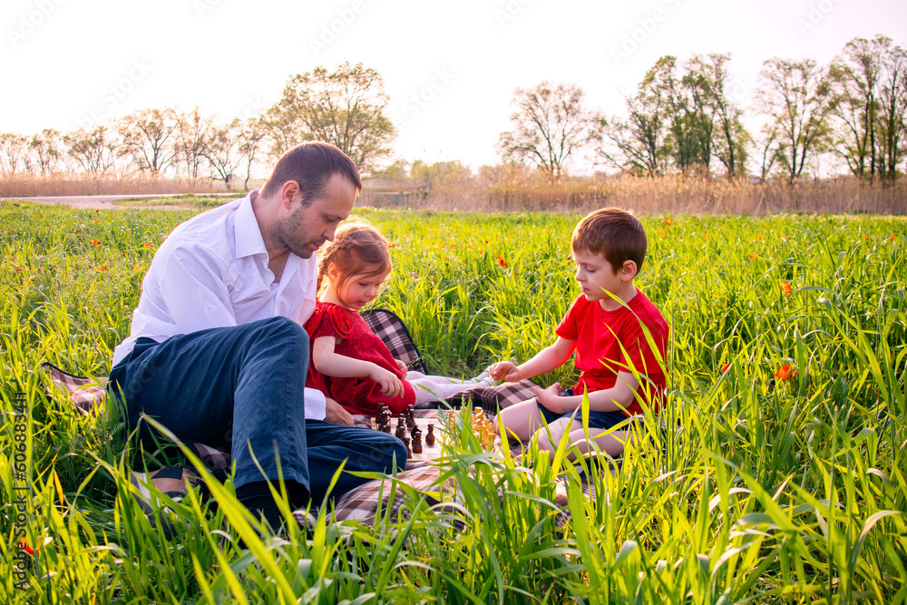 father and children. dad and son play chess on a picnic father and children. dad and son play chess on a picnic