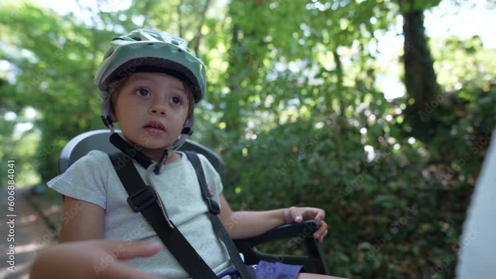 Child in bike back seat with helmet riding nature pathway outdoors. Little boy rides bicycle with mother in forest Child in bike back seat with helmet riding nature pathway outdoors. Little boy rides bicycle with mother in forest