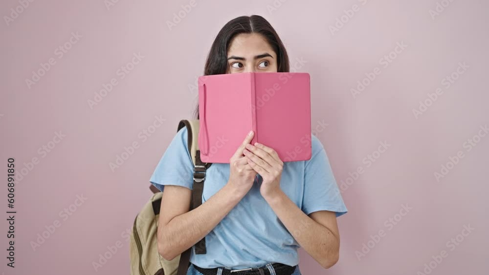 Young beautiful hispanic woman student covering face with book over isolated pink background Young beautiful hispanic woman student covering face with book over isolated pink background