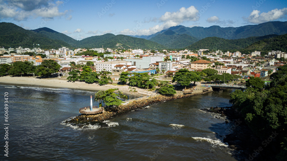 Aerial drone view of a Brazilian coastal city, with the beach in the foreground and the historic center in the background, with a navigation lighthouse and river estuary on a sunny day - Ubatuba