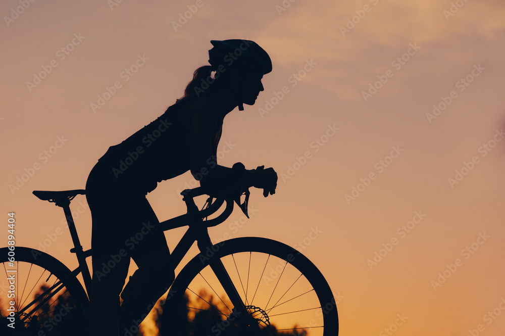 Obraz premium Silhouette of a woman riding a bike during a sport cycling race on a sunset