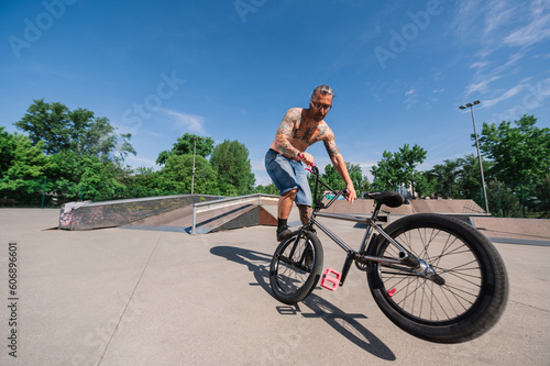 Wide angle view of a professional bmx rider covered with tattoos doing extreme sports in a skate park.