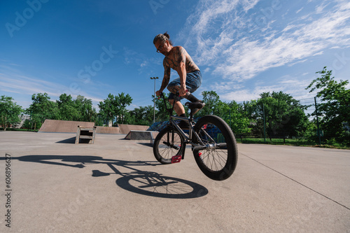 An active oldish man is performing freestyle bike tricks on his bmx in a skate park.