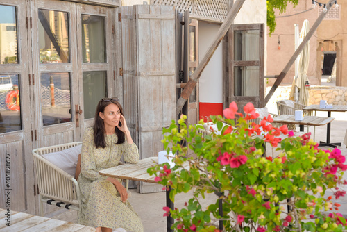 A young woman sits in a street cafe and enjoys the views of the old city of the Emirates. Deira, Burdubai. © Ekaterina