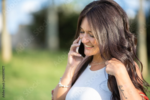 Close-up view of a happy woman smiling while talking on the phone outdoors on a sunny day.