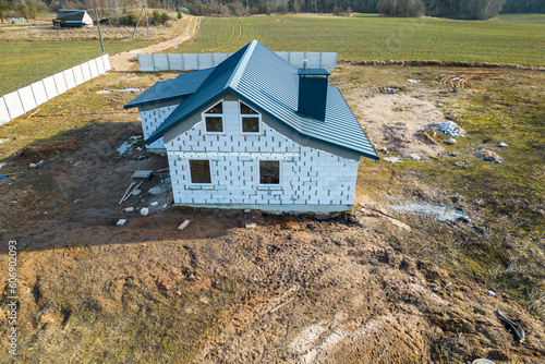 Construction and repair of country houses. New cottage with double-glazed windows on the plot. Aerial view from a drone to a construction site in a field. Construction of social housing.