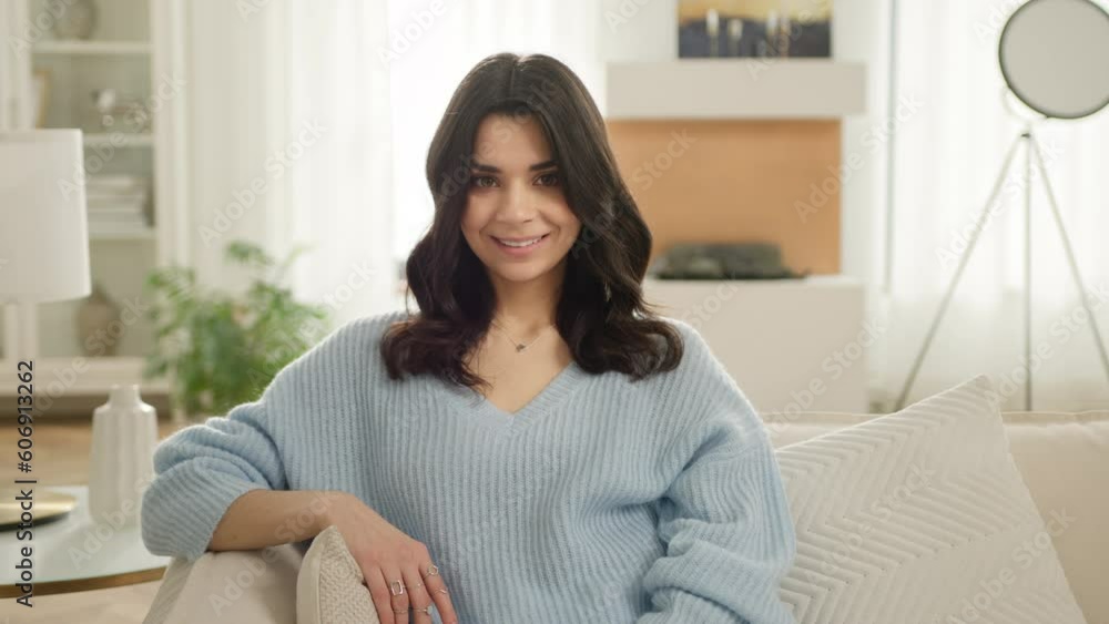 Happy young latina woman feels satisfied posing for portrait view in living room modern apartment, slow motion people. Smiling beautiful hispanic woman looking at camera sitting on sofa alone at home Happy young latina woman feels satisfied posing for portrait view in living room modern apartment, slow motion people. Smiling beautiful hispanic woman looking at camera sitting on sofa alone at home