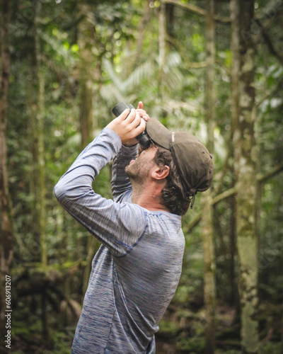 Turista com binóculos na mão observando pássaros na floresta amazônica, em alta floresta, mato grosso