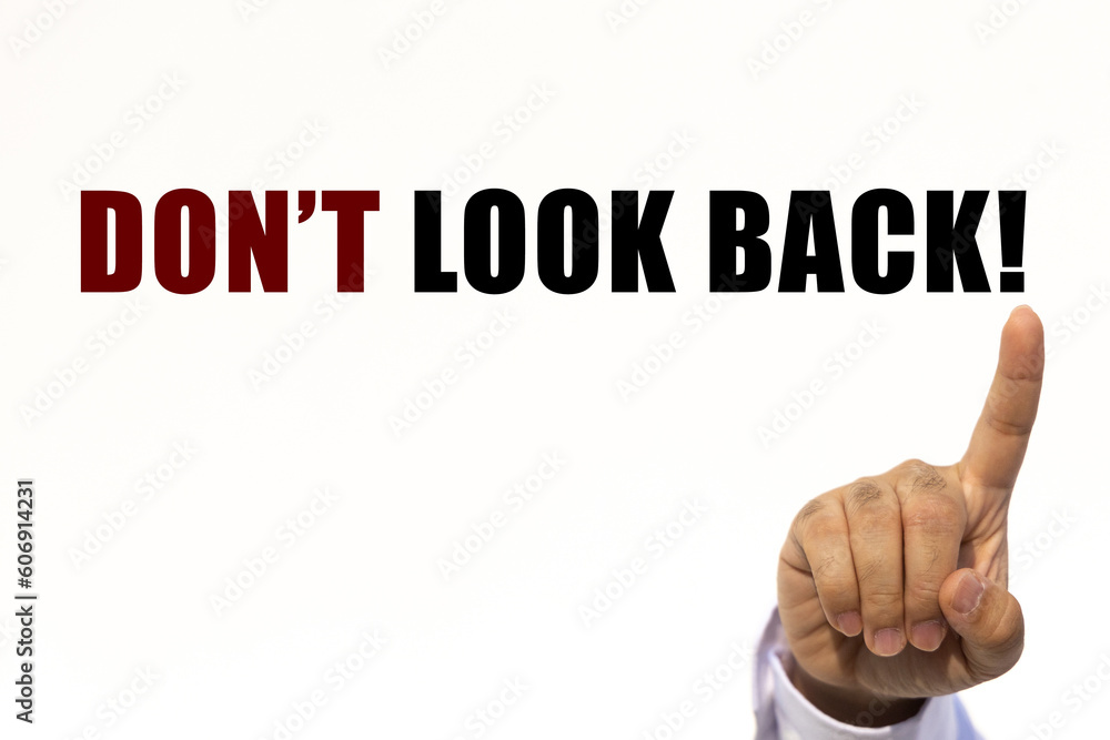Don't look back text on white wall background with businessman's finger point at the message with empty space. This message can be used as business concept about don't look back. Don't look back text on white wall background with businessman's finger point at the message with empty space. This message can be used as business concept about don't look back.