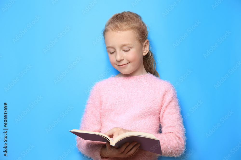 Happy little girl reading book on light blue background Happy little girl reading book on light blue background