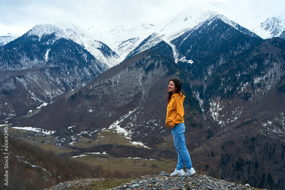 A girl in a yellow jacket and blue jeans enjoys the cold mountain scenery of snow-covered mountains