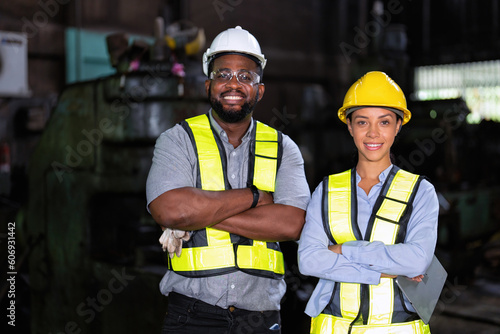 Female worker and coworker posing confidently while standing with arms crossed in factory workshop 