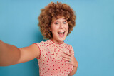 Smiling lady with afro hairstyle in spotted top posing on blue background, making selfie, happy moments concept, copy space