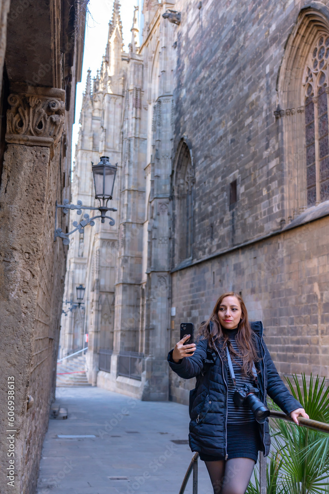 Peaceful young woman tourist in casual outfit with photo camera walking in Gothic Quarter against arched passage during sightseeing trip in Barcelona, Spain